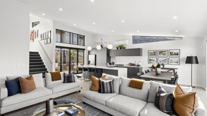 A modern open-plan living area with a kitchen, dining space, and a staircase leading to an upper level. - Highview Hideaway -  stunning lake and mountain views. (Queenstown)