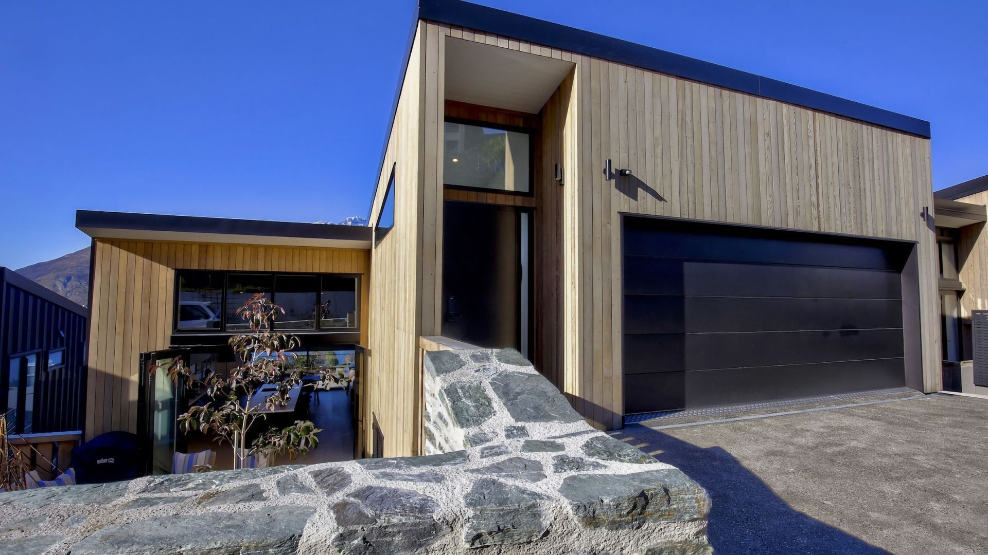Ein modernes Haus mit Naturstein-Fassade, einer Garage und Holzverkleidung.