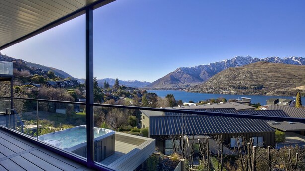 A modern house with a large glass window, a hot tub, and a view of a lake and mountains. - Highview Hideaway -  stunning lake and mountain views. (Queenstown)