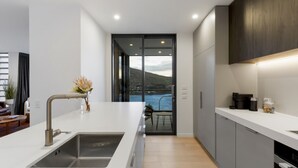 A modern kitchen with a large island, a built-in sink, and a view of a lake through large windows. - Belle Vue Villa - Stunning Views with Hot Tub (Queenstown)
