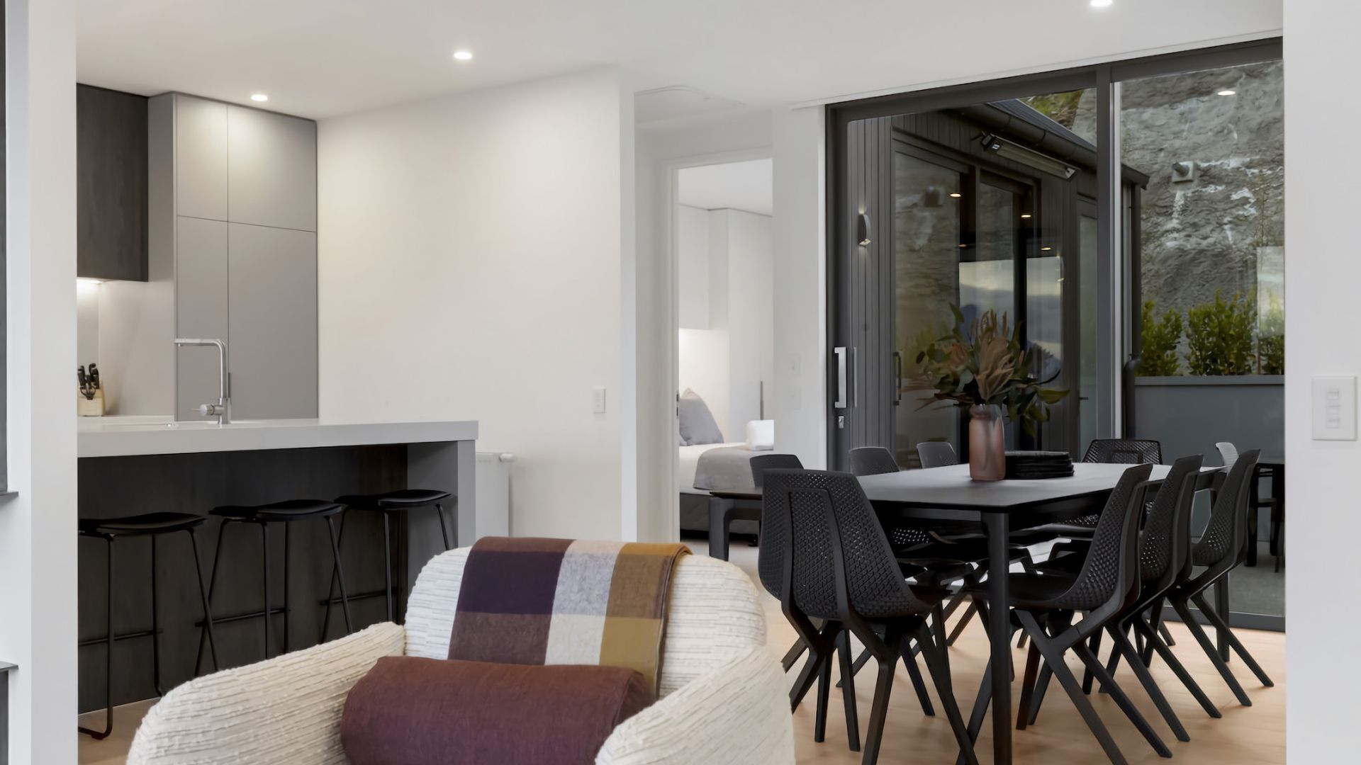 Une cuisine moderne avec des tabourets de bar, un coin repas avec une table et des chaises, et une grande fenêtre donnant sur un paysage verdoyant.