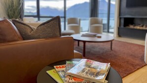 A modern living room with a leather sofa, a coffee table with magazines, and a view of the sea through large windows. - Belle Vue Villa - Stunning Views with Hot Tub (Queenstown)