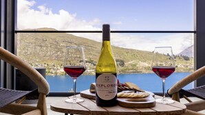 A bottle of wine and two glasses on a table with a scenic view of a lake and mountains. - Belle Vue Villa - Stunning Views with Hot Tub (Queenstown)