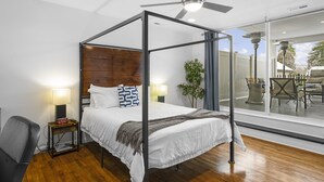 Una cama con dosel, cabecera de madera, lámparas de noche, un reloj digital y vistas del patio exterior a través de una puerta de cristal.