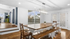 Un comedor con mesa y bancos de madera, paredes blancas y vistas al exterior.