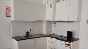 A compact kitchen with white cabinets, a black countertop, a coffee maker, and a dishwasher. - Tanoeiros Studios (Funchal)