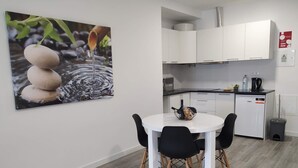 A modern kitchen with white cabinets, a small refrigerator, and a dining area with a white table and black chairs. - Tanoeiros Studios (Funchal)