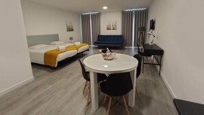 A hotel room with a bed, a blue sofa, a dining table with chairs, and a lamp. - Tanoeiros Studios (Funchal)