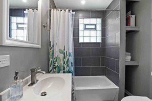 A bathroom with a white sink, a shower with a curtain, and a small window. - A Dream Home in Chicagoland (Homewood)