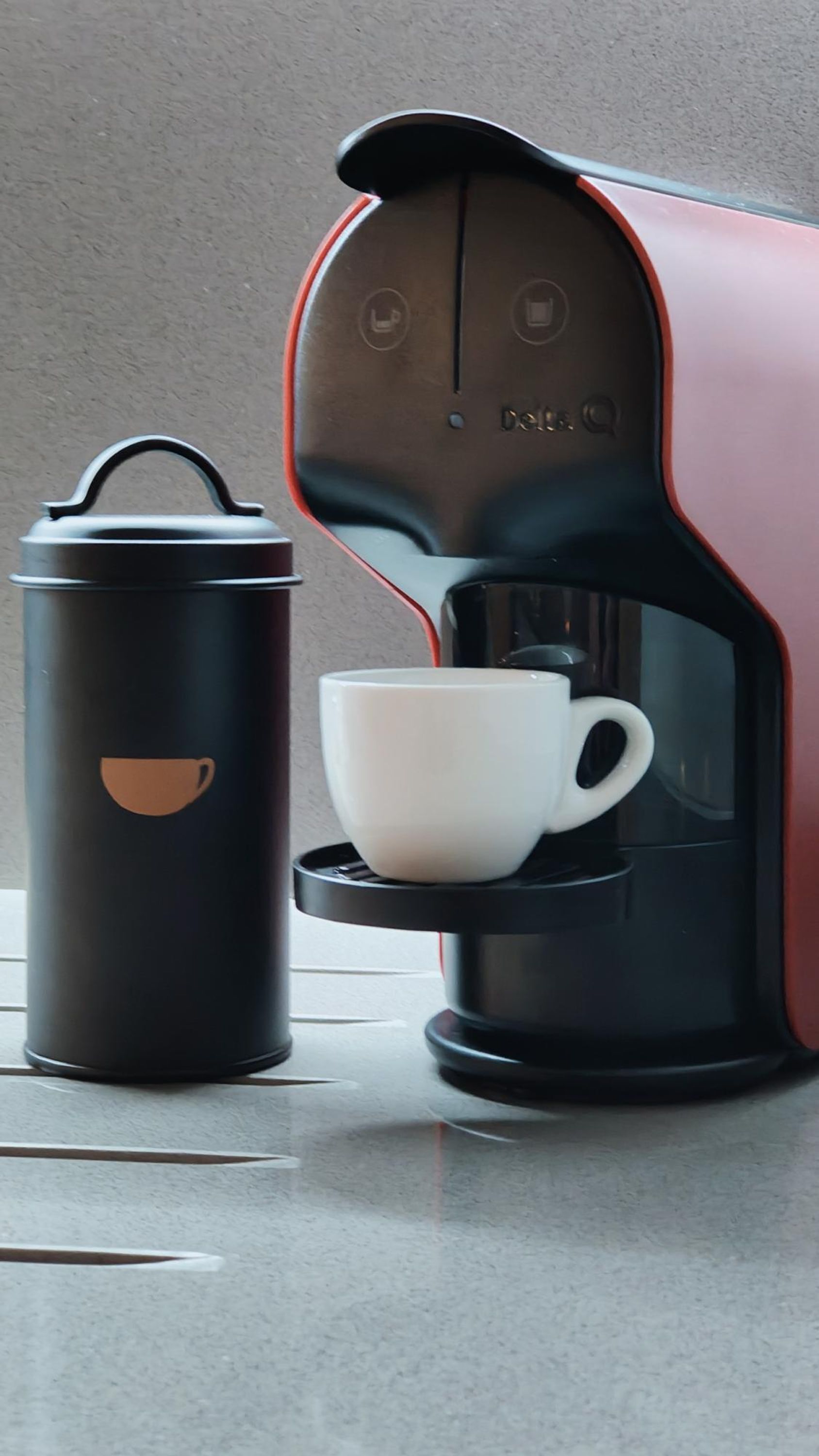 A coffee maker with a cup and a thermos on a countertop.