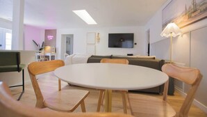A modern living room with a round table, wooden chairs, a sofa, a flat-screen TV, and a floor lamp.