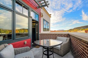 Une terrasse extérieure avec une table et des chaises, un bâtiment rouge et une vue sur un paysage vallonné.