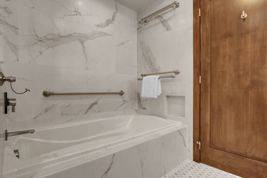 A bathroom with a marble wall, a bathtub, a wooden door, and a towel rack.