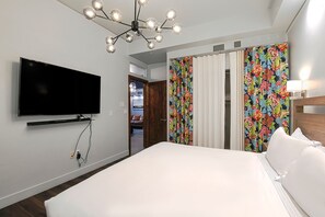 A hotel room with a large bed, a flat-screen TV mounted on the wall, and a ceiling light fixture.