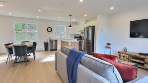 Une cuisine moderne dotée d’un îlot central, d’un coin repas avec des chaises et d’un canapé agrémenté d’un plaid bleu.