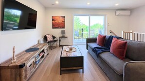 Un salon moderne doté d’un téléviseur à écran plat, d’un canapé avec des coussins rouges, d’une table basse en bois et d’un balcon aménagé avec du mobilier d’extérieur.