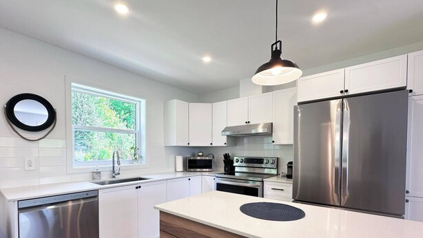 Une cuisine moderne avec des meubles blancs, des appareils en acier inoxydable et un élément décoratif en bois sur l’îlot central.
