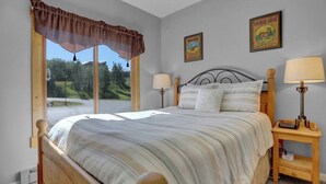 Une chambre avec un grand lit, deux tables de chevet avec des lampes, une fenêtre donnant sur un paysage verdoyant et deux tableaux encadrés accrochés au mur.