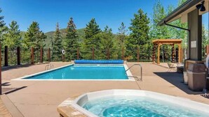 Une piscine avec un jacuzzi, entourée d’une pergola en bois et d’un espace clos, avec des arbres en arrière-plan.