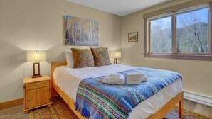 A bedroom with a bed, two bedside lamps, a window with a view, and a painting on the wall. - Pines Peak Place Summ (Steamboat Springs)
