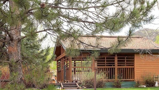 A wooden cabin with a covered porch, surrounded by pine trees and a stone pathway leading to the entrance. - Pines Peak Place Summ (Steamboat Springs)