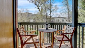 A wooden deck with a round table and two chairs, overlooking a scenic view of hills and trees. - Pines Peak Place Summ (Steamboat Springs)
