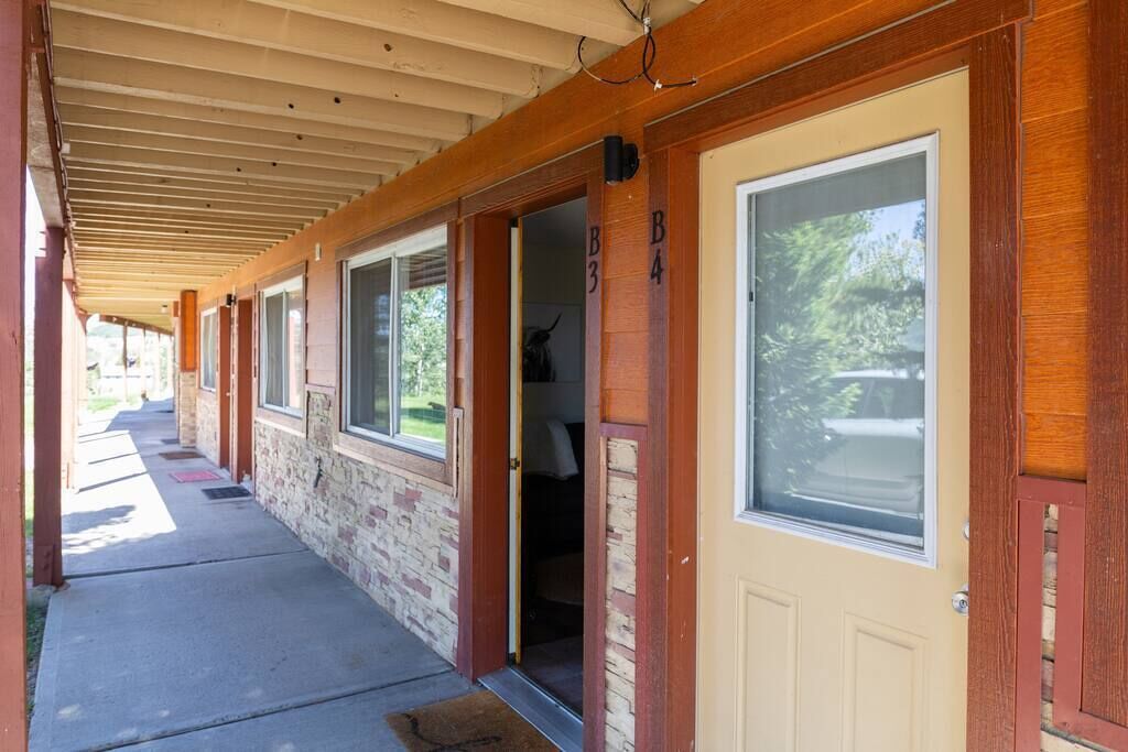 Un porche couvert, doté de portes et de fenêtres en bois, qui mène à un bâtiment en briques.