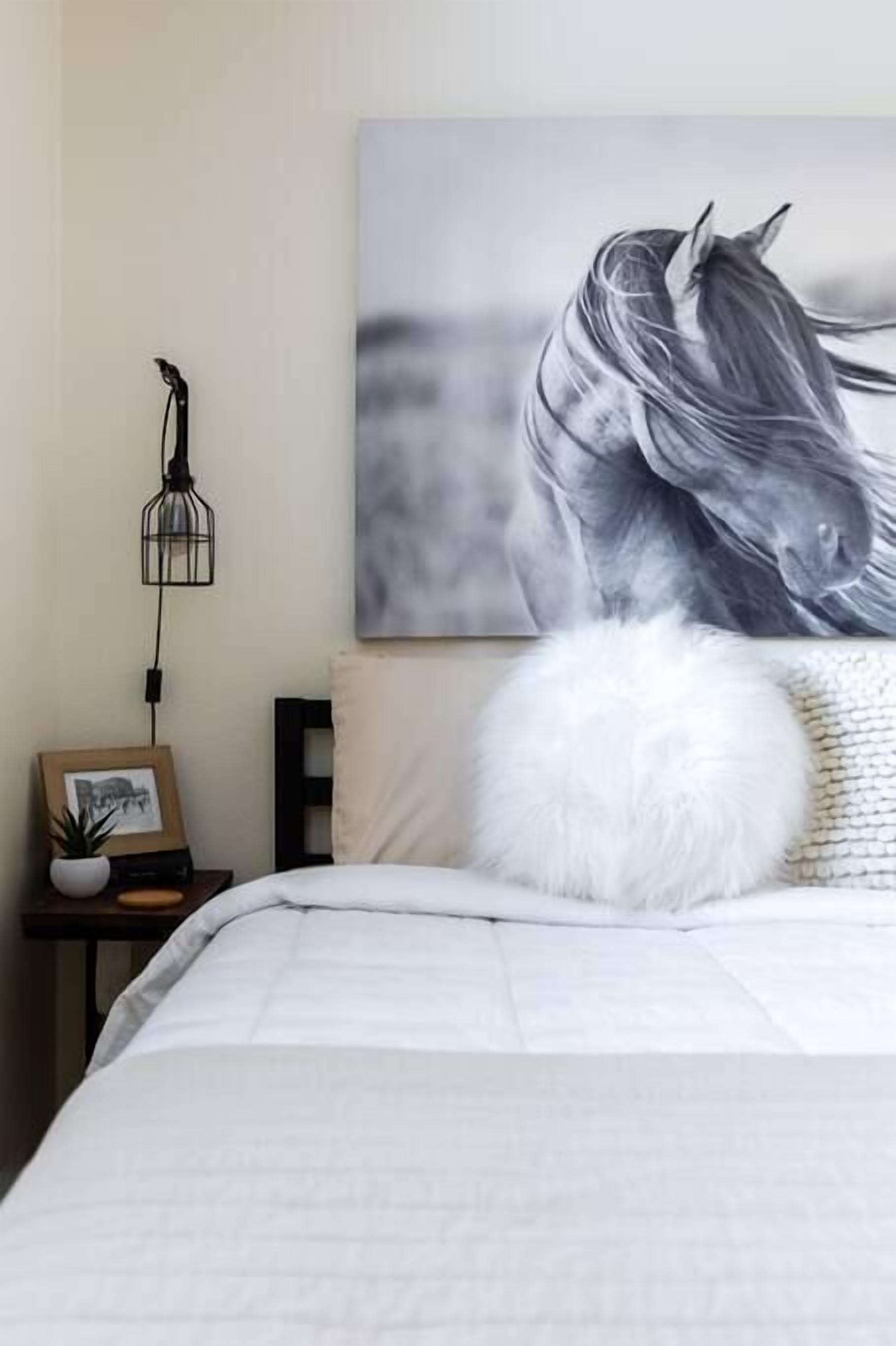 Un dormitorio con una cama grande, un cuadro enmarcado sobre una mesita de noche, una lámpara colgante y un cuadro grande en la pared.