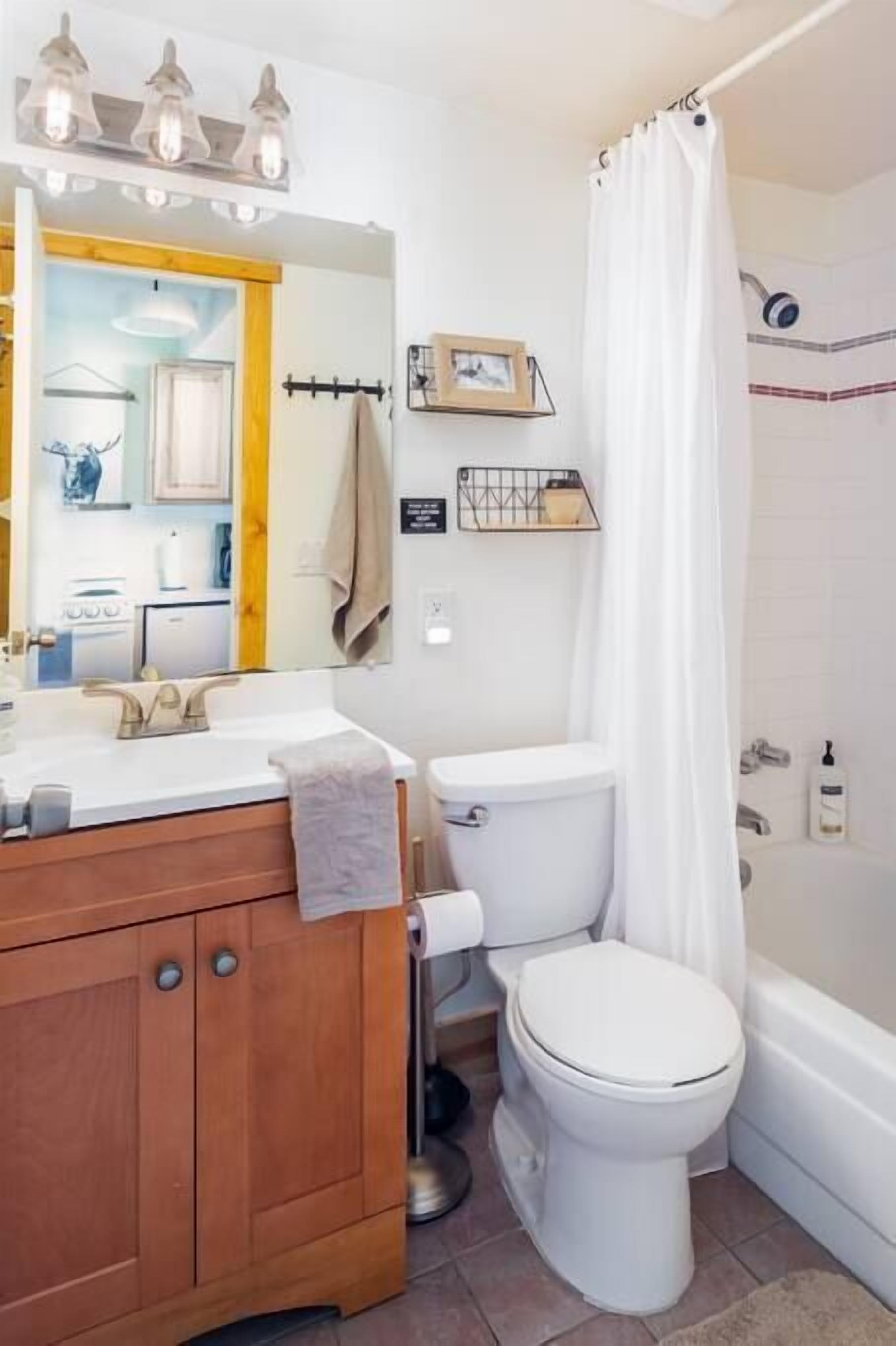 Un bagno con un mobile vanitario in legno, un water bianco, una tenda da doccia e uno specchio con illuminazione.