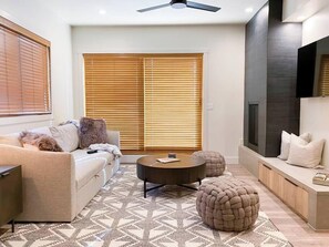 Un salon moderne avec un canapé, une table basse ronde, un pouf et un téléviseur.