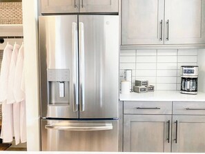 A stainless steel refrigerator with a water dispenser, a coffee maker, and a clock on the countertop.
