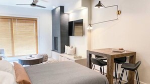 A modern hotel room with a bed, a desk, two chairs, a TV, and a ceiling fan. - Sunset Retreat (Steamboat Springs)