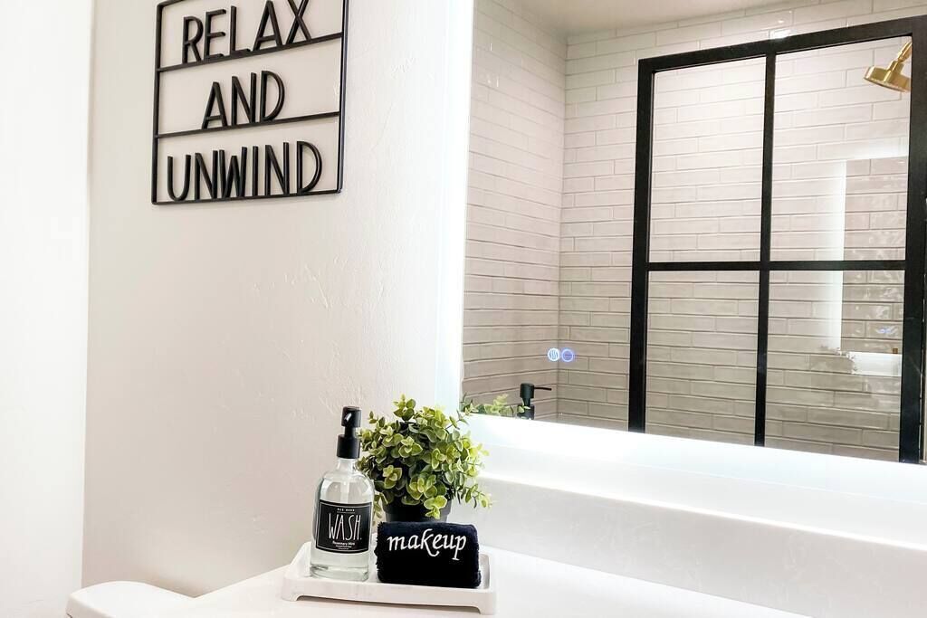 A bathroom with a white bathtub, a black towel with 'makeup' written on it, a bottle of hand soap, and a potted plant.