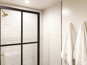 Un baño con azulejos blancos tipo metro, una puerta de ducha de vidrio con marco negro y dos toallas blancas colgadas en la pared.