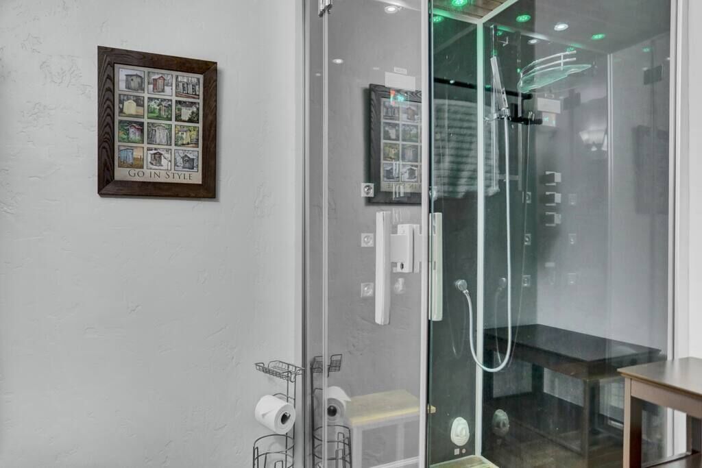 Ein modernes Badezimmer mit Duschkabine aus Glas, einem gerahmten Bild an der Wand und einem kleinen Tisch.