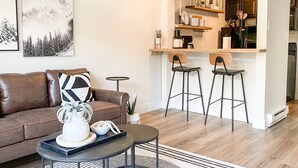 Een moderne woonkamer met een bruine leren bank, een salontafel, en een keuken met een bar en krukken.