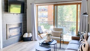 Een moderne woonkamer met een open haard, een flatscreen televisie, een bank, een salontafel en een balkon met buitenmeubilair.