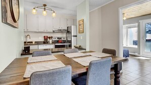 Une cuisine moderne avec des meubles blancs, une table à manger en bois et quatre chaises, ainsi qu’un luminaire suspendu.