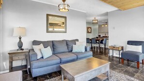 Un salon moderne avec un canapé gris, une table basse et, au fond, un coin repas.