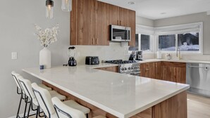 A modern kitchen with a large island, wooden cabinets, stainless steel appliances, and a view of the outdoors.