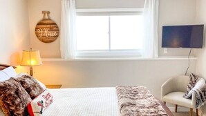 Une chambre à coucher comprenant un lit, une chaise, un téléviseur, une fenêtre avec des rideaux et un élément de décoration murale.