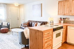 Un espacio habitable compacto con kitchenette, un sofá, una mesa de centro y un tapete estampado.