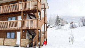 Un bâtiment en bois à plusieurs étages, doté de balcons et d’un escalier, avec un paysage enneigé en arrière-plan.