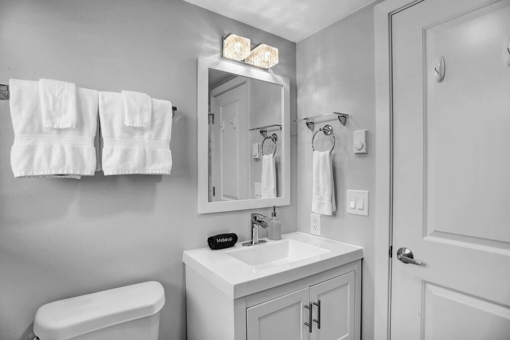 A bathroom with a white sink, a mirror with lights, and towels hanging on the wall.