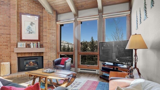 A cozy living room with a fireplace, large windows, and a comfortable seating area. - Rustic Ridgetop Retreat (Steamboat Springs)