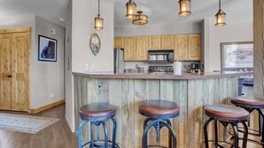 A kitchen with wooden cabinets, a central island, and three bar stools. - Rustic Ridgetop Retreat (Steamboat Springs)