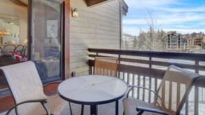 A balcony with a round table and four chairs, overlooking a snowy landscape with buildings in the background. - Rustic Ridgetop Retreat (Steamboat Springs)