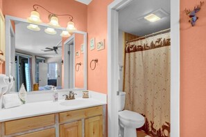 A bathroom with a white sink, wooden cabinets, a large mirror, and a shower curtain with a forest and deer design.