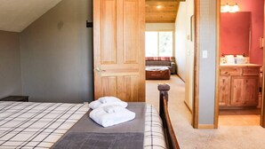 Een slaapkamer met een bed, een houten deur naar een badkamer en uitzicht op een zithoek.