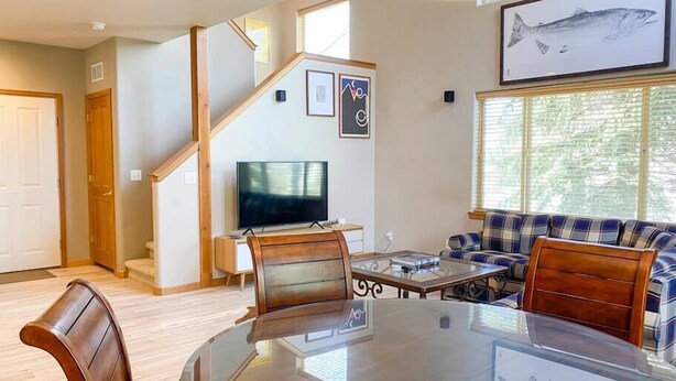 Een moderne woonkamer met een eettafel met glazen blad, houten stoelen, een bank, een televisie en kunstwerken in lijsten.
